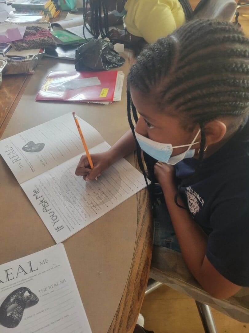Child writing at desk, wearing a mask.