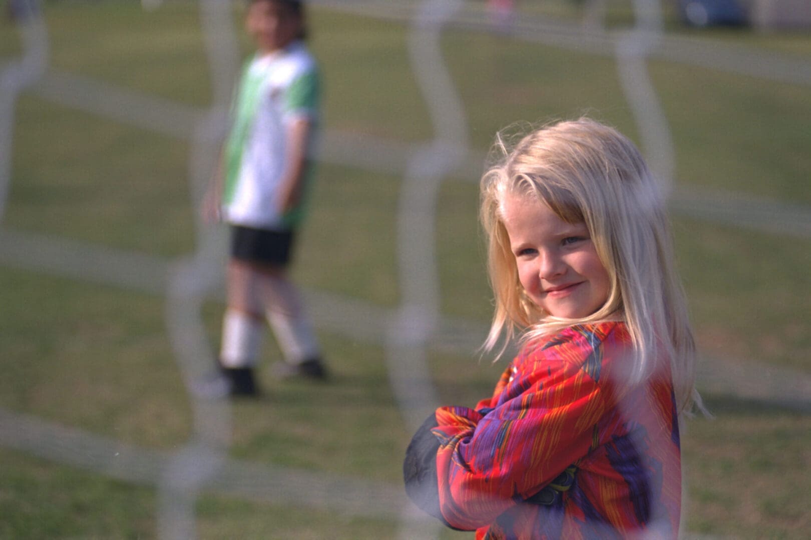 Girl smiling through soccer goal netting.