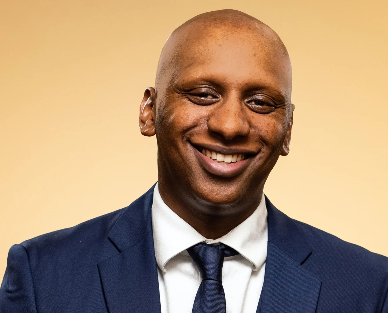 Smiling man in suit with beige background.