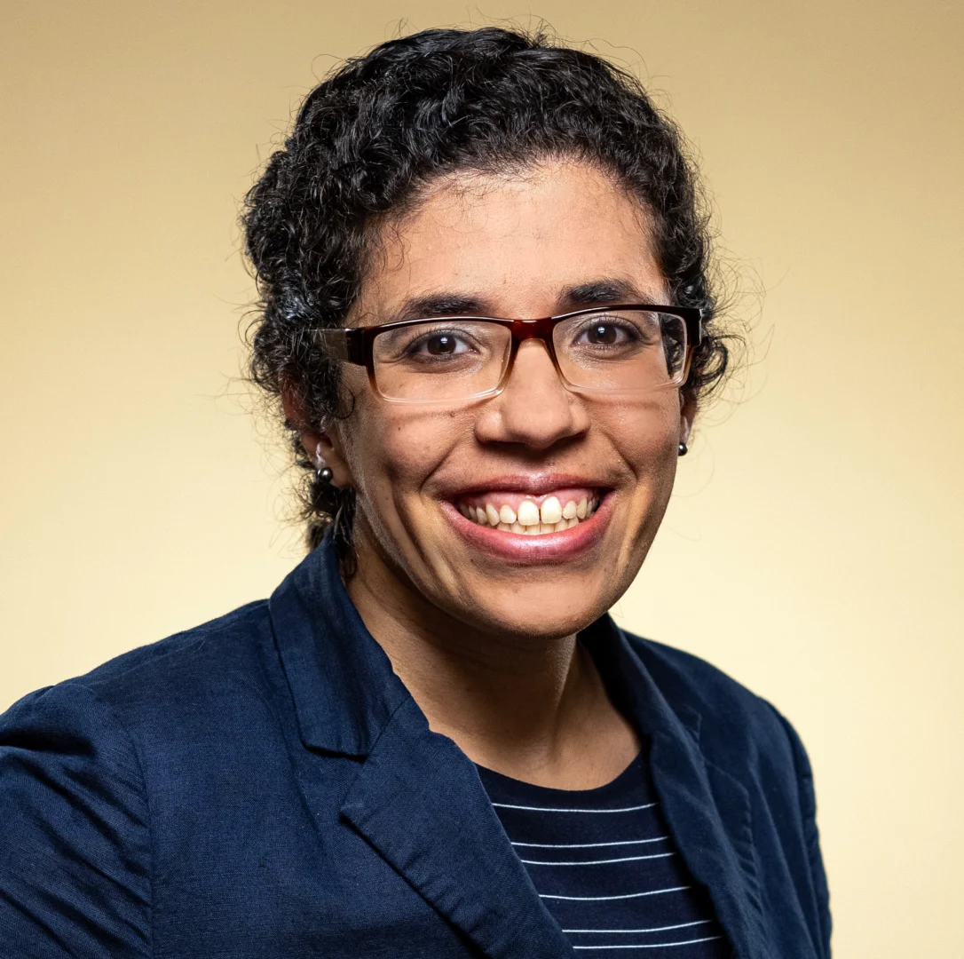 Smiling person wearing glasses and a suit.