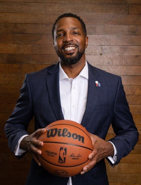 Man in suit holding a basketball, smiling.