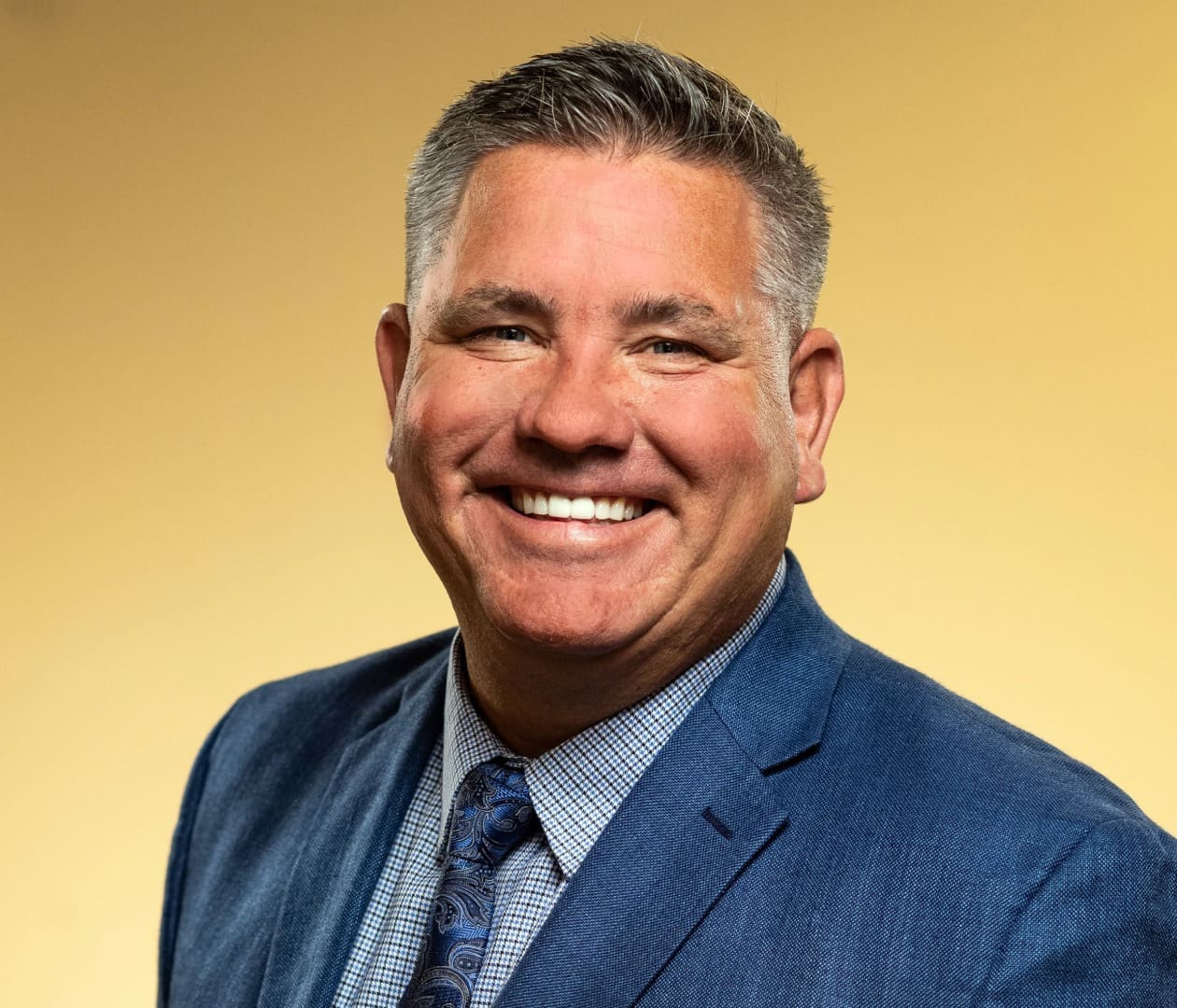 Smiling man in blue suit, yellow background.