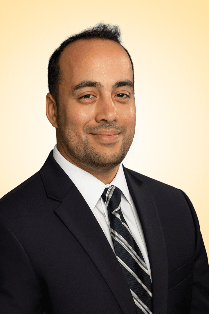 Man in suit smiling against yellow background.